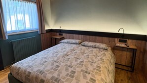 Une chambre à coucher avec un lit, une table de chevet, une fenêtre avec des rideaux et des poutres en bois au plafond.