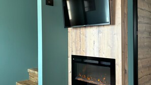 A modern interior with a flat-screen TV mounted on a wooden wall, a built-in fireplace below it, and a staircase leading to another level. - Baita Miralago - Salient with Mountain Views, Shared Garden, and Wi-Fi (Livigno)