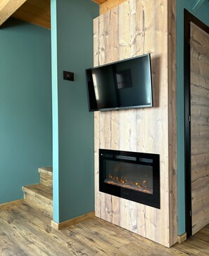 A modern interior with a flat-screen TV mounted on a wooden wall, a built-in fireplace below it, and a staircase leading to another level. - Baita Miralago - Salient with Mountain Views, Shared Garden, and Wi-Fi (Livigno)