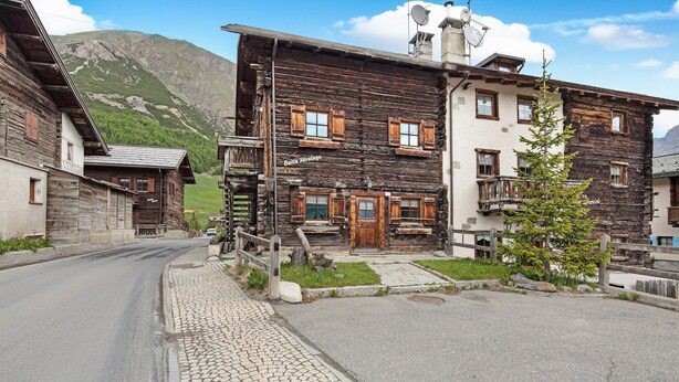 Ein traditionelles Holzhaus mit Balkon, einem Kopfsteinpflasterweg und einer Bergkulisse.