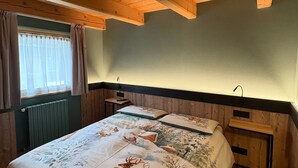 A room with a wooden ceiling, a bed with a deer-themed bedspread, a nightstand, and a window with curtains. - Baita Miralago - Salient with Mountain Views, Shared Garden, and Wi-Fi (Livigno)