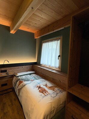 A room with a bed, a window with curtains, a bedside table, and a wooden ceiling.