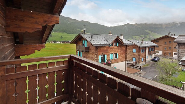 Ein Holzbalkon mit Blick auf ein Dorf mit traditionellen Häusern und einem Berg im Hintergrund.