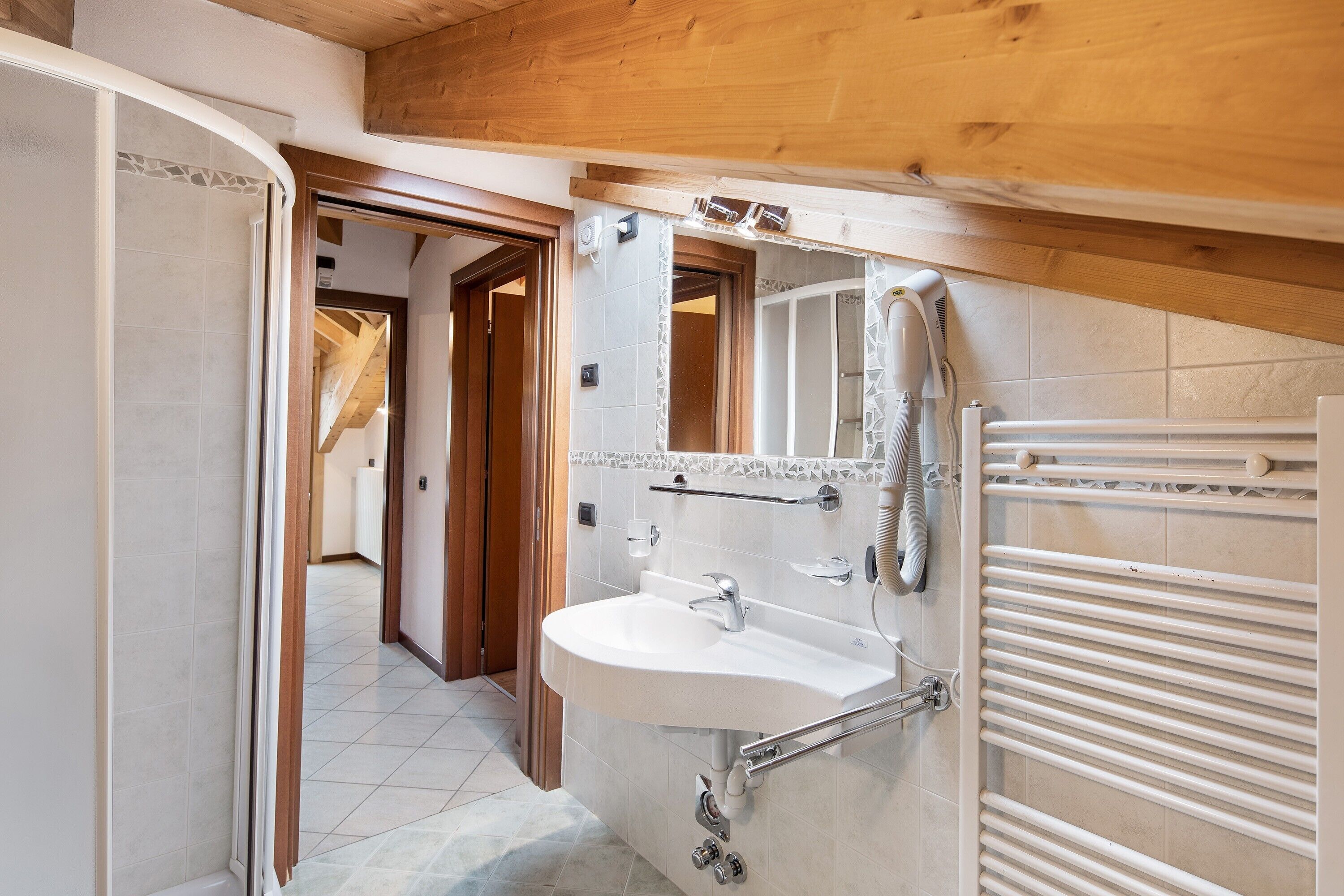 Un baño con lavamanos blanco, toallero y zona de ducha.