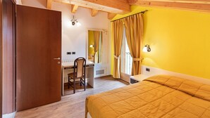 Ein Zimmer mit einem Bett, einem Schreibtisch, einem Sessel, einem Spiegel und einer Tür.