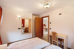 Ein Schlafzimmer mit einem Bett, einem Schreibtisch, einem Stuhl, einem Spiegel und einer Tür zu einem Badezimmer.
