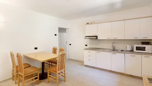A compact kitchen with white cabinets, a microwave, a sink, and a dining table with chairs.
