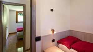 A bedroom with a bed, a bedside table, a wall-mounted light, and a door leading to another room.