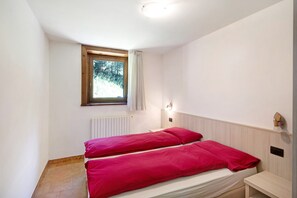 A small, single-bed room with a window, a radiator, and a bedside table.