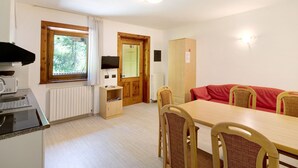 A room with a wooden dining table, chairs, a red sofa, a wooden cabinet, a television, and a window with curtains.