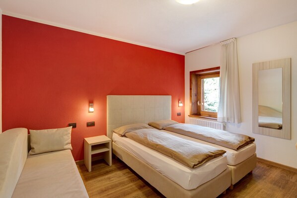 Une chambre avec deux lits, une table de chevet, une fenêtre avec des rideaux et un miroir au mur.