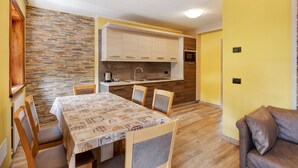 A compact kitchen with a built-in oven, a dining area with a table and chairs, and a yellow wall. - Apartment Baita Belvedere - Teola with Mountain View, Balcony and Wi-Fi (Livigno)