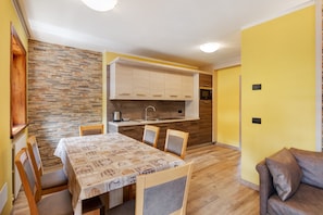 Une cuisine compacte dotée d’un four encastré, un coin repas avec une table et des chaises, et un mur jaune.
