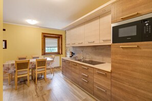 Une cuisine avec des meubles en bois, un four à micro-ondes Siemens, un évier et un coin repas comprenant des chaises et une table.
