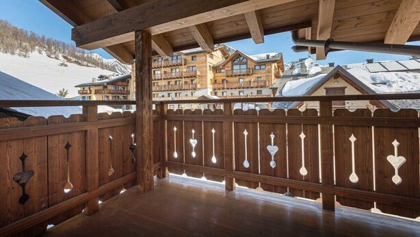 Un balcon en bois offrant une vue sur des bâtiments enneigés et une montagne en arrière-plan.