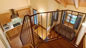 Un escalier menant à une chambre à coucher avec une couvre-lit à motifs, une cuisine dotée de meubles en bois et un four à micro-ondes.