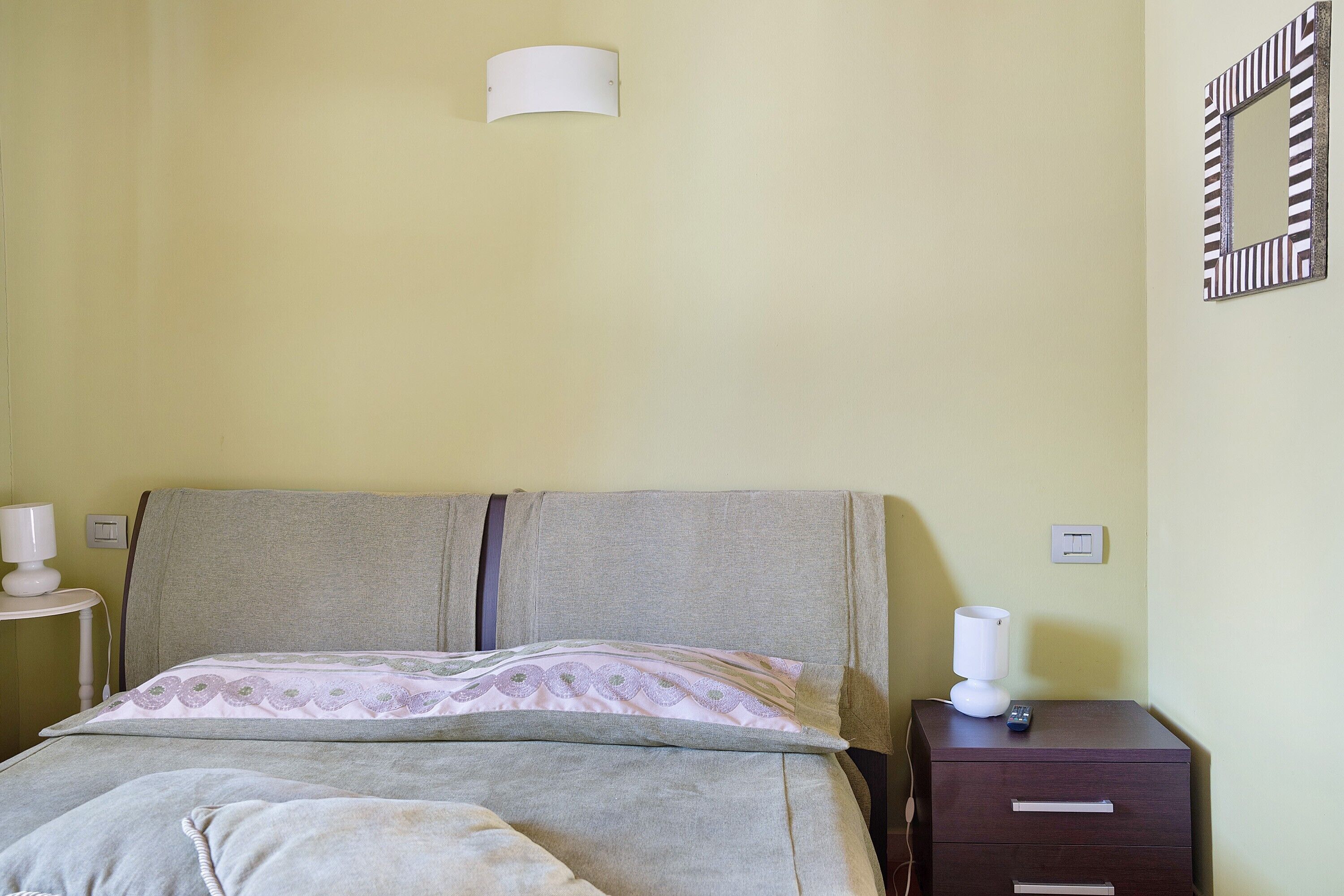 A bed with a headboard, a bedside table with a lamp, a nightstand, and a drawer unit.