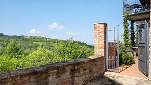 Un muro de piedra, una reja metálica y vistas de colinas verdes.