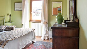 A bedroom with a bed, a dresser, a mirror, a window with curtains, and a radiator.