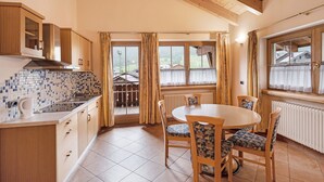 A kitchen with a tiled backsplash, wooden cabinets, a dining table with chairs, and a view through the windows. - Apartment 'Miky House Valandrea' with Mountain View, Balconies and Wi-Fi (Livigno)