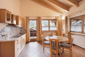 A kitchen with a tiled backsplash, wooden cabinets, a dining table with chairs, and a view through the windows.