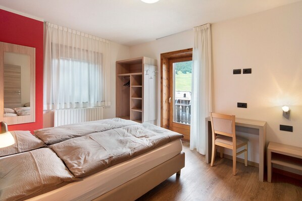 A bedroom with a bed, a desk, a chair, a wardrobe, and a window with curtains.