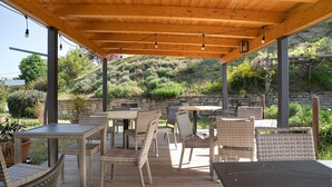 Eine Terrasse im Freien mit Korbmöbeln, einer Holzbalkendecke und einer Steinwand im Hintergrund.