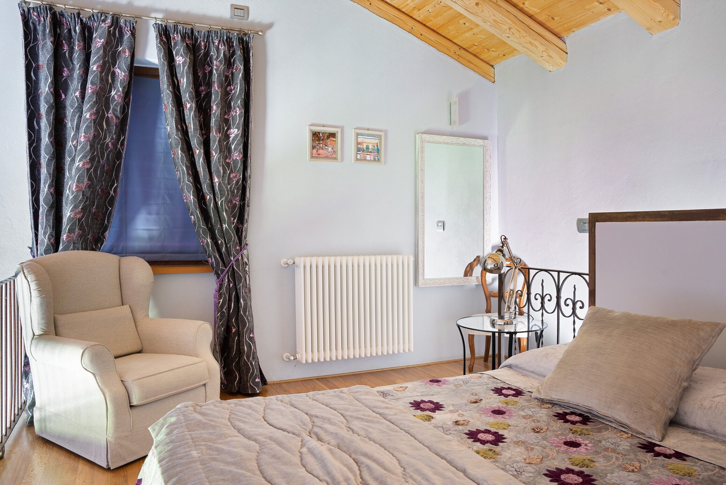 A bedroom with a bed, a chair, a radiator, and a window with curtains.