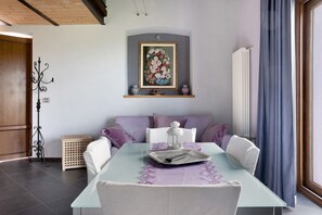 Un comedor con una mesa preparada para dos personas, un cuadro colgado en la pared y una ventana con cortinas.