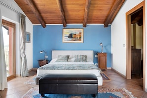 Una camera da letto con soffitto in legno, un letto con testiera bianca, un comodino, una lampada e un quadro appeso al muro.