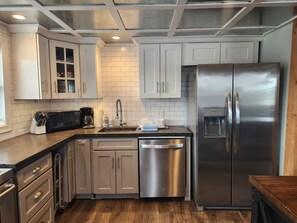 A modern kitchen with stainless steel appliances, white cabinetry, and a wooden floor.