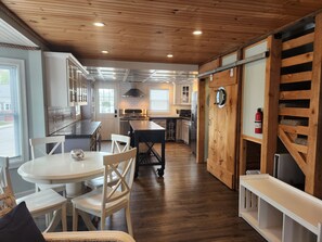 A modern kitchen with wooden accents, a dining area with white furniture, and a fire extinguisher mounted on the wall.