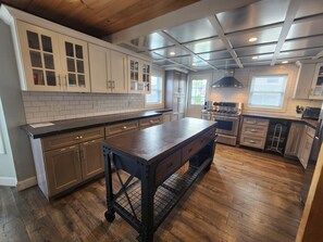 Une cuisine moderne dotĂ©e dâun grand Ăźlot central, dâappareils Ă©lectromĂ©nagers en acier inoxydable et dâun plafond en bois.