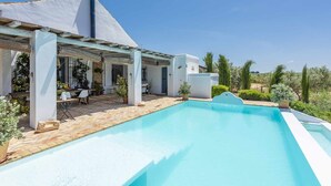 Ein Poolbereich mit überdachter Terrasse, Sitzgelegenheiten im Freien und Blick auf die umliegende Landschaft.