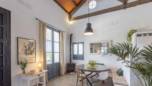 Ein Essbereich mit einem runden Tisch, Stühlen und einer Couch. Ein Fenster mit Vorhängen, ein wandmontierter Spiegel und eine Pendelleuchte sind vorhanden.