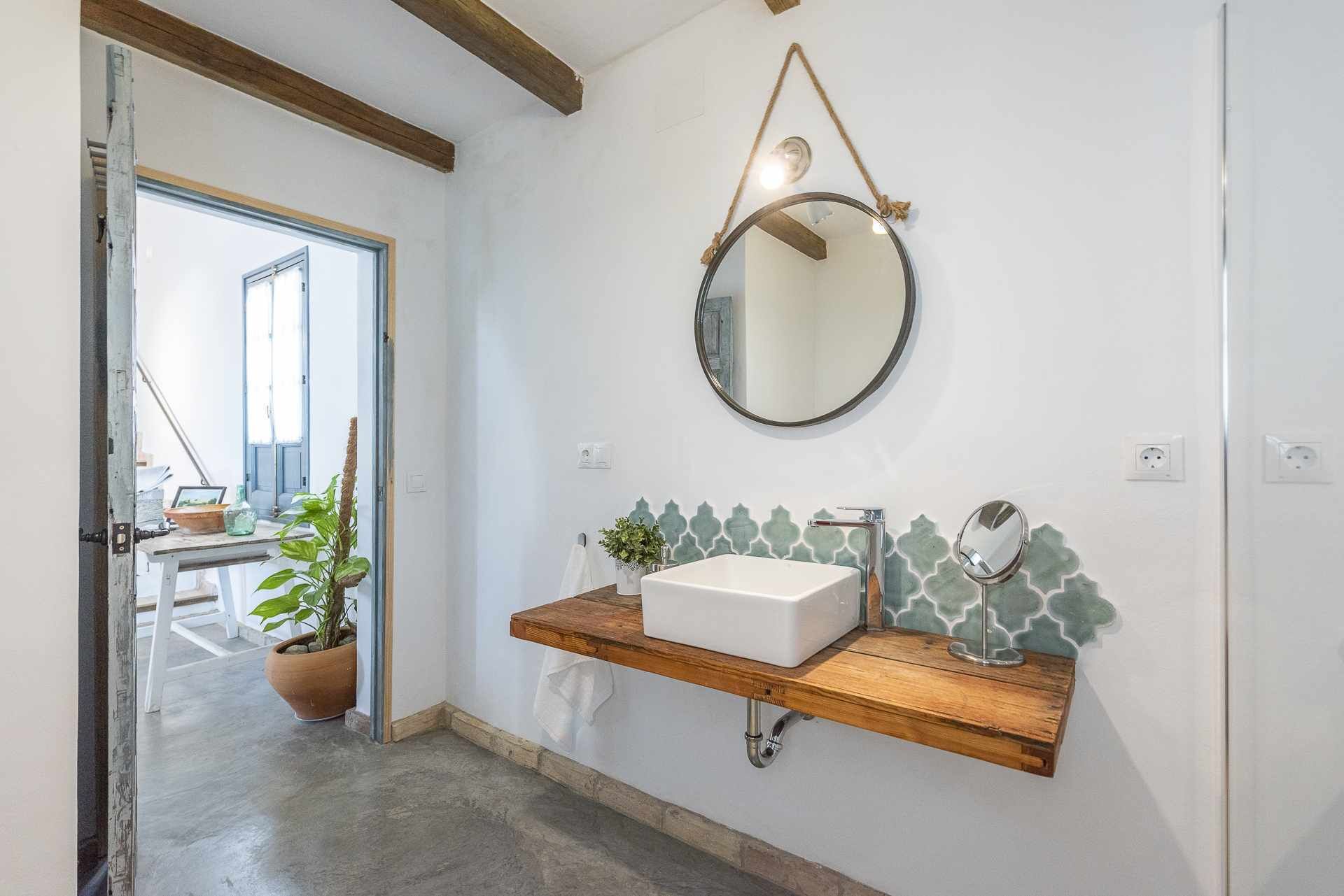 A bathroom with a wooden vanity, a white sink, a mirror, and a potted plant.