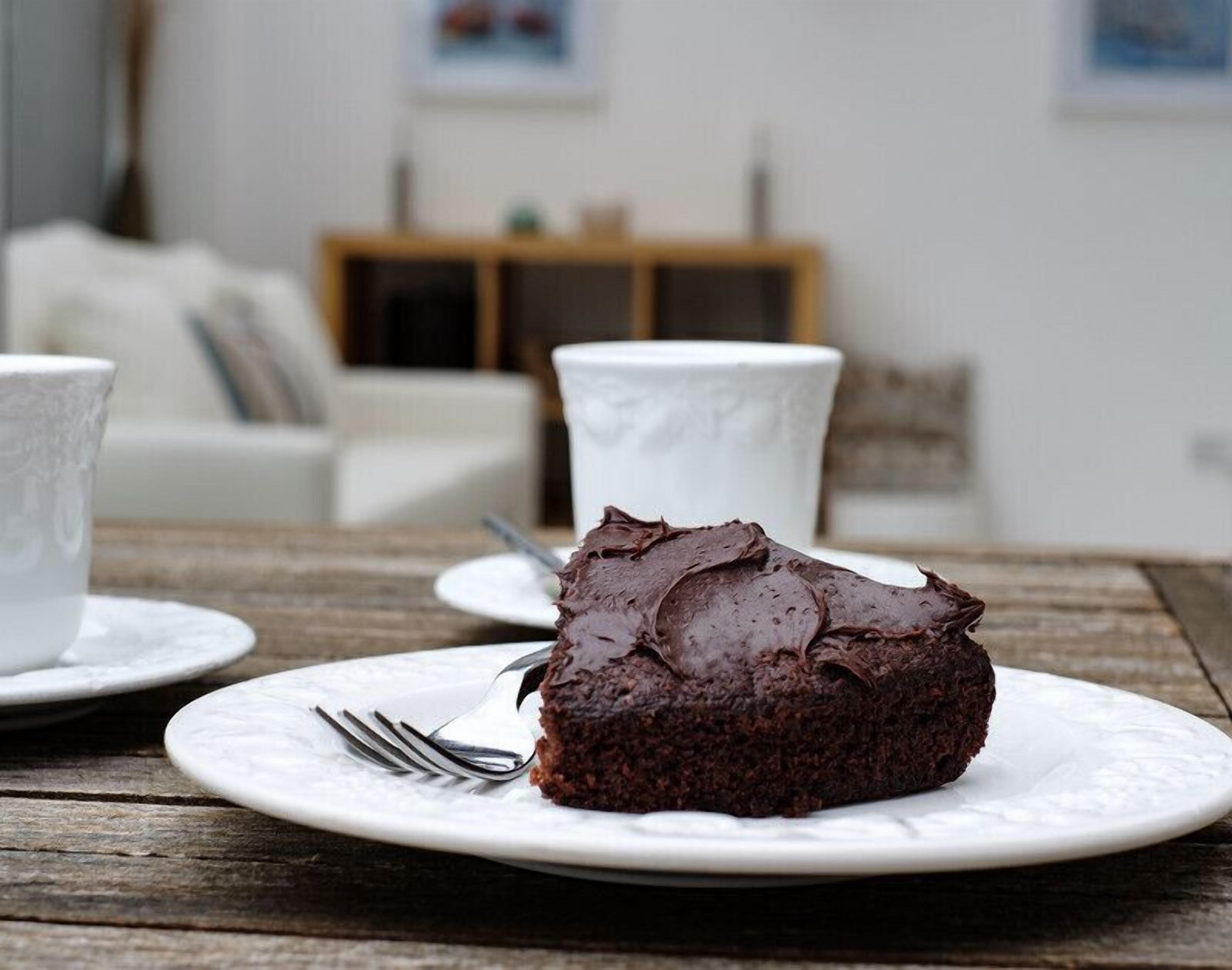 Una rebanada de pastel de chocolate sobre un plato blanco, con un tenedor a un lado, colocada sobre una mesa de madera.