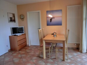 A dining area with a table and chairs, a television on a cabinet, a clock, and a painting on the wall.