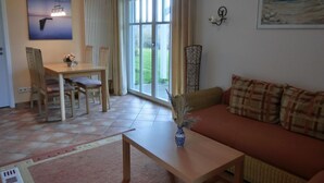 Un salón con sofá, una mesa de centro, una mesa de comedor con sillas, un cuadro y vistas a través de la puerta de vidrio.