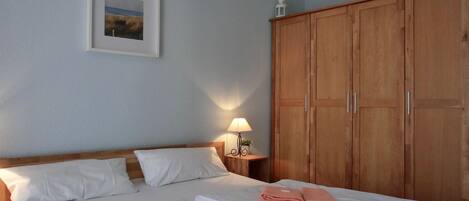 Ett hotellrum med en stor säng, en garderob i trä, ett nattduksbord med en lampa och en inramad tavla på väggen.