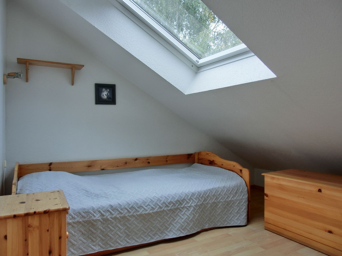Una habitación pequeña con una cama individual, techo inclinado y tragaluz.