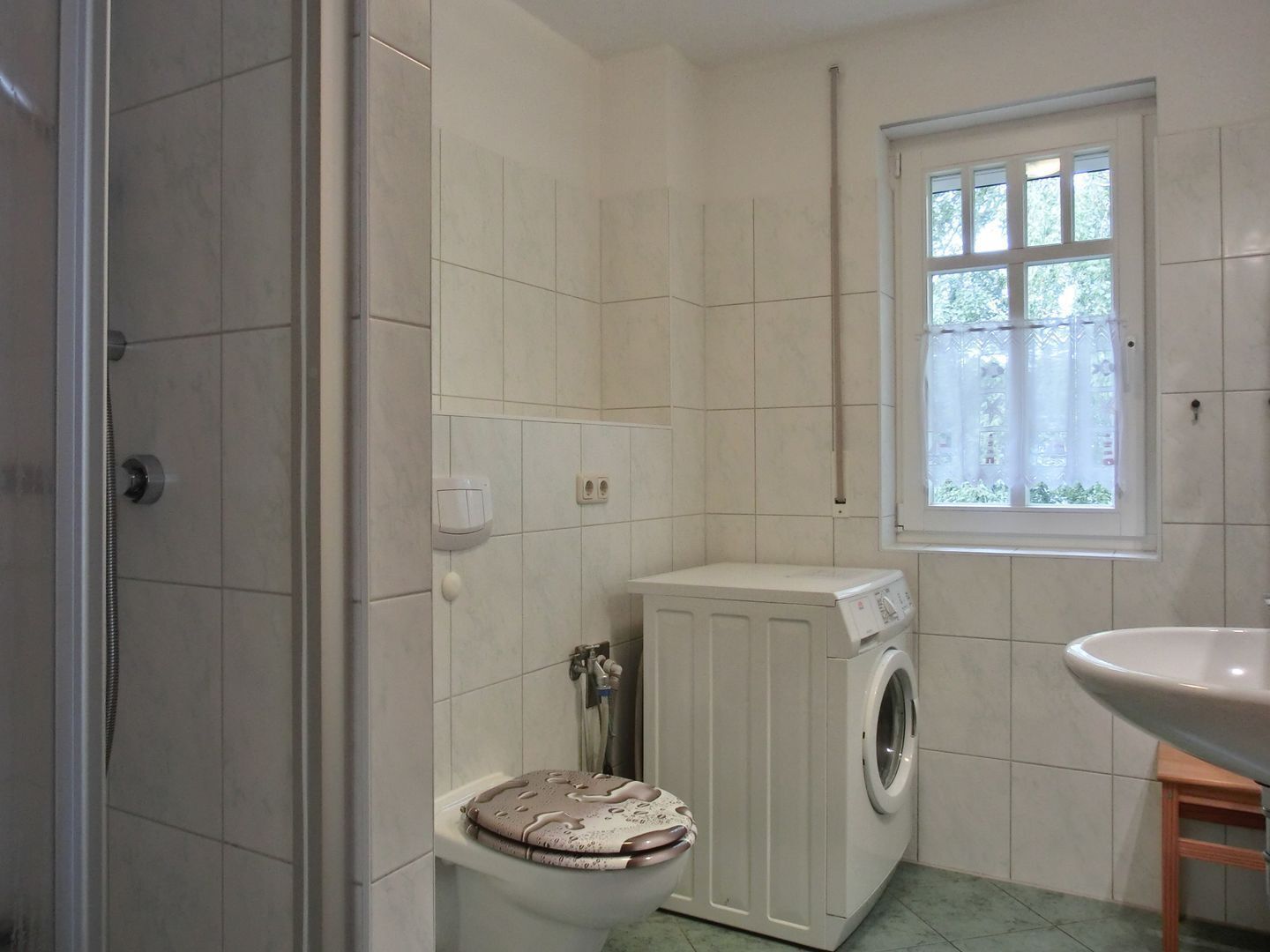 Baño con inodoro, lavadora, lavabo y ventana.