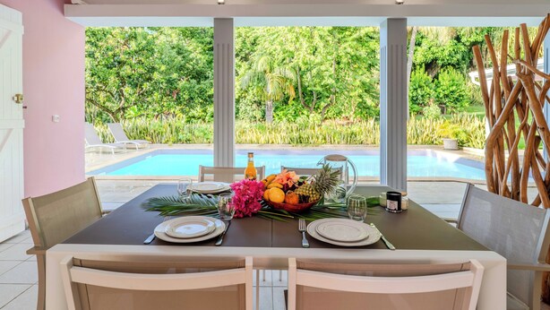 A dining table set for two with a tropical fruit bowl, a bottle, and a glass. - Magnificent Zen Villa with swimming pool in a 4000 m2 garden (Bouillante)