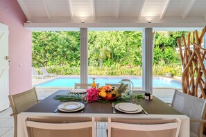 Une table dressée pour un dîner à deux, avec un saladier rempli de fruits tropicaux, une bouteille et un verre.