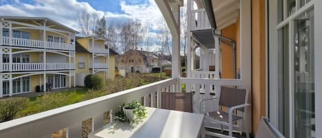 A balcony with a table and chairs, overlooking a courtyard with multiple buildings.