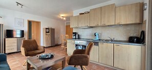 A modern kitchen with wooden cabinets, a gas stove, and a coffee machine. There is a dining area with two chairs and a table.