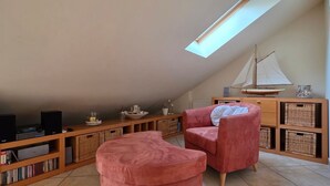 Un dormitorio tipo loft acogedor con techo inclinado, tragaluz, una maqueta de velero, una estantería y dos sillas rosadas.