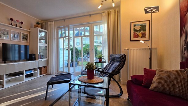 A modern living room with a flat-screen TV, a glass coffee table, a black leather armchair, and a red sofa.
