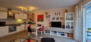 A modern kitchen with white cabinets, a built-in oven, and a dining area with red chairs.