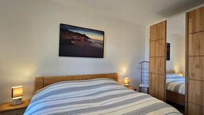 Een slaapkamer met een bed, bedlampjes, een houten garderobe en een lijst met een afbeelding aan de muur.